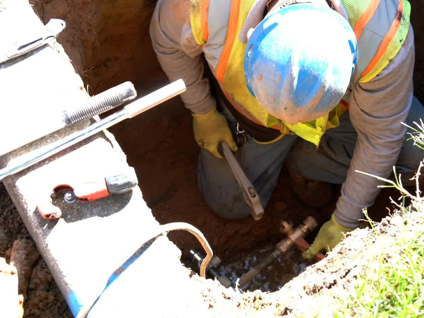 Worker exposing a buried line in a small dig at the curb, drain cleaning