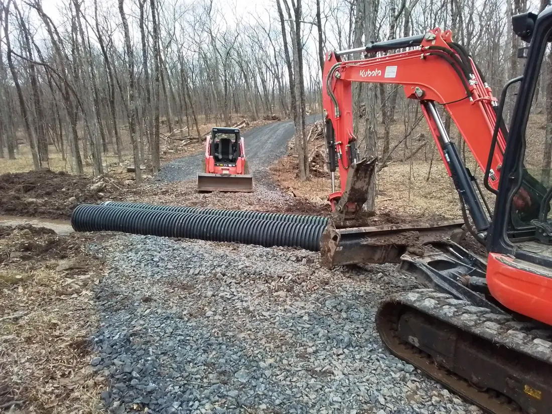Drainage systems work setting a corrugated culvert pipe across a gravel driveway