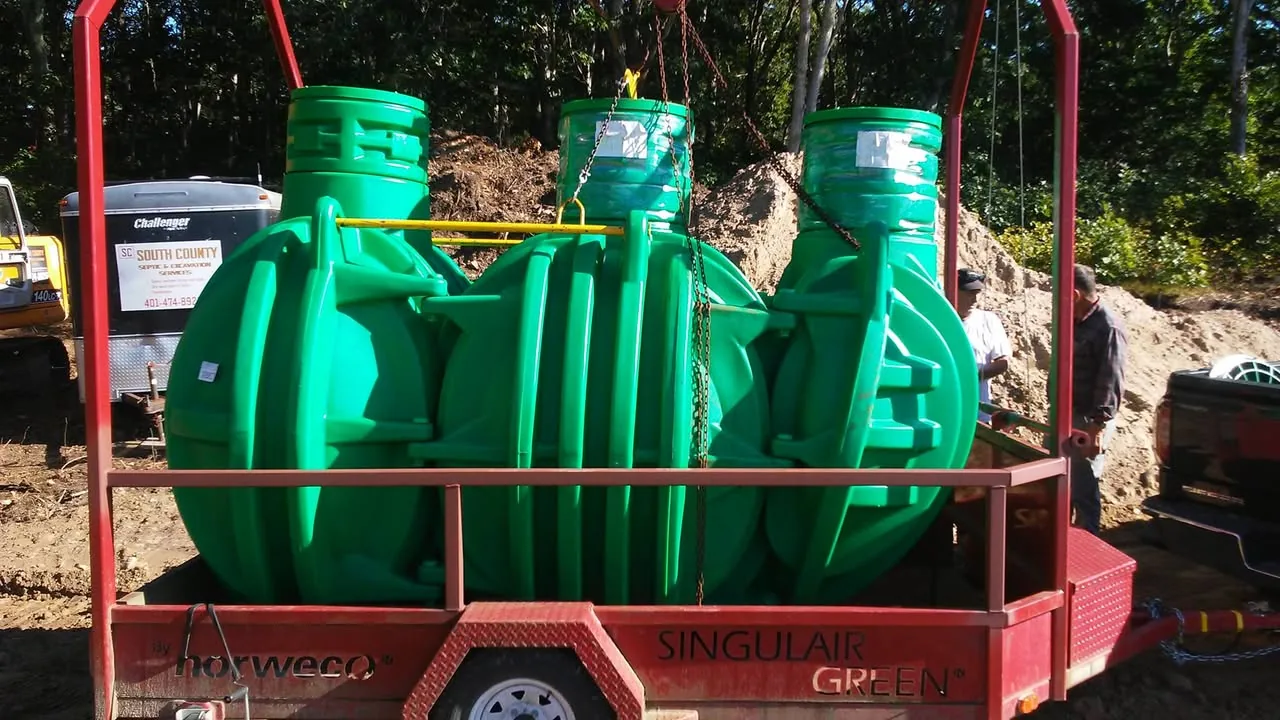 Septic system installation with three new green treatment tanks on a trailer beside the dig