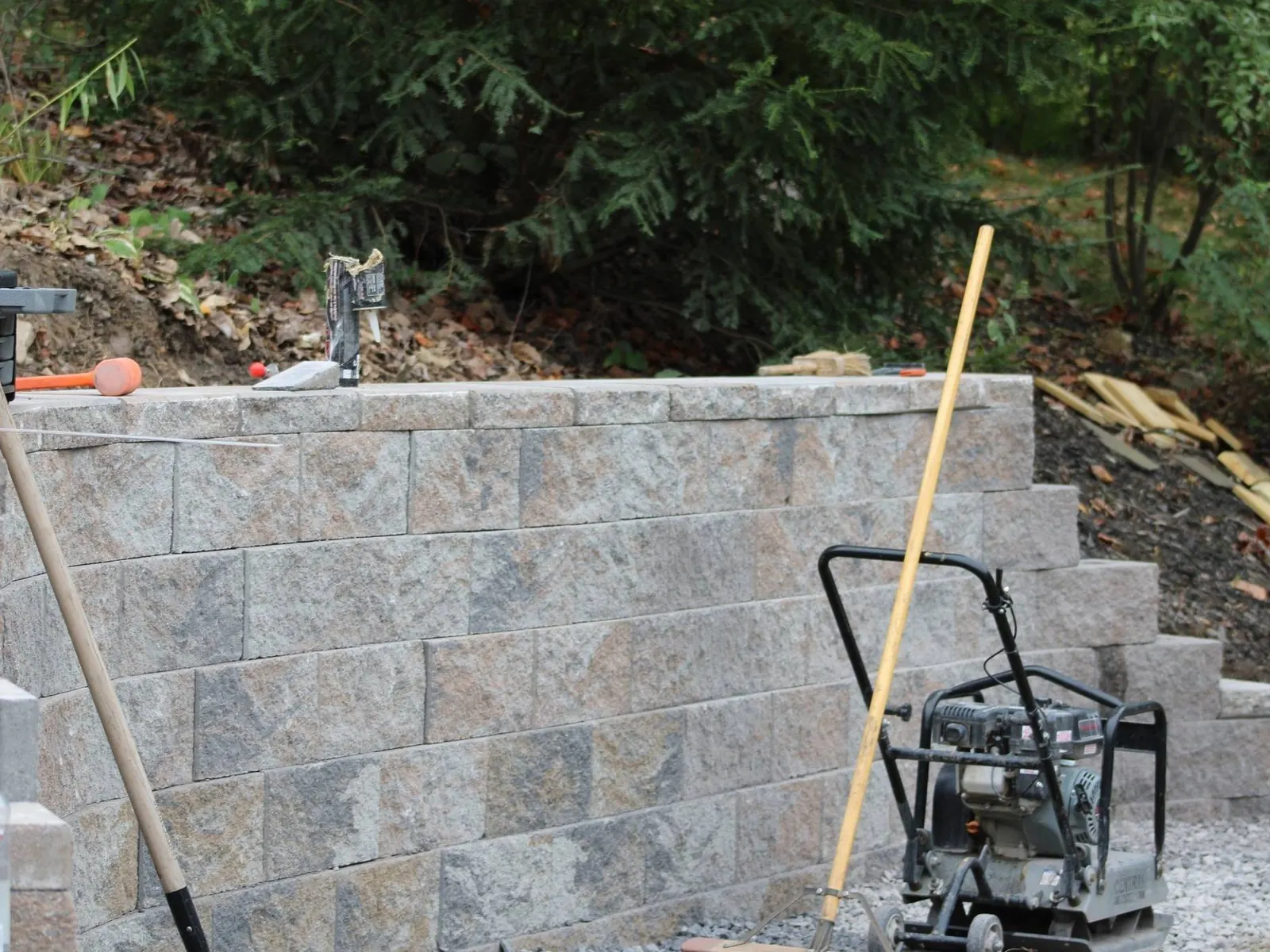 Retaining walls under construction with block courses, a plate compactor and a shovel