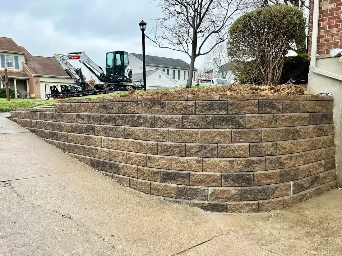 Retaining walls of stacked block along a driveway with a mini excavator behind