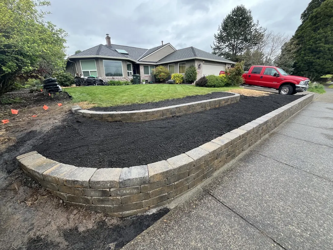 Retaining walls of curved block along a walkway, backfilled with dark soil