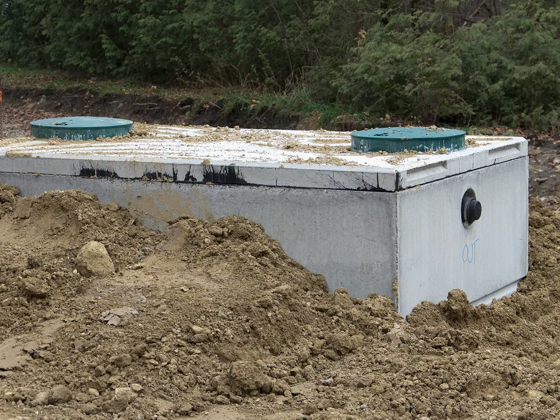 Septic system repair with a new concrete tank and two green lids set in the dig