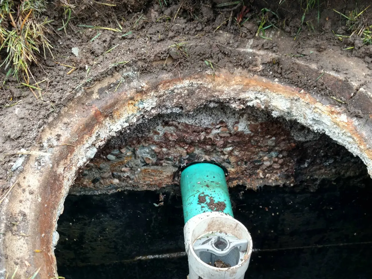 Septic system repair with an opened concrete tank showing the green outlet pipe and filter