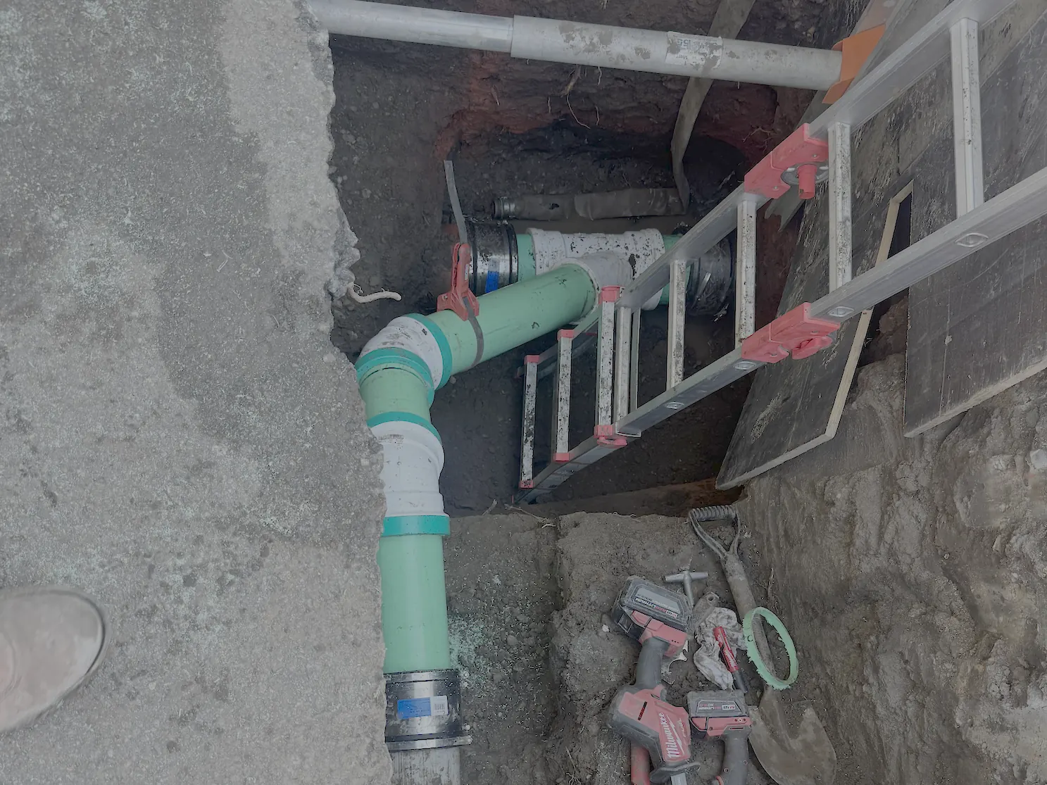 Sewer line repair pit with new green PVC pipe and fittings joined to the old line