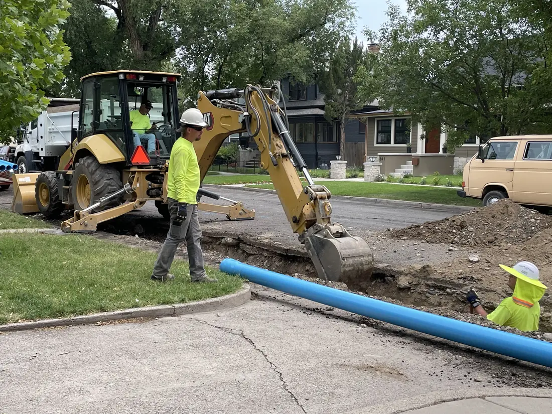 Water line repair with a backhoe digging at the curb and new blue pipe laid out